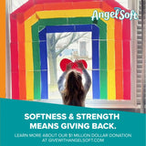 Person holding a heart-shaped object in front of a colorful window display with 'Angel Soft' branding.