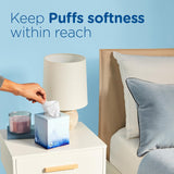 Hand reaching for a tissue box on a nightstand next to a bed with a blue background.
