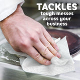 Hand cleaning a surface with text 'TACKLES tough messes across your business' on a blurred background