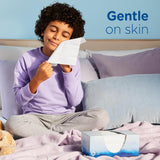 Child holding a tissue with a box of tissues on a bed, emphasizing 'Gentle on skin'.